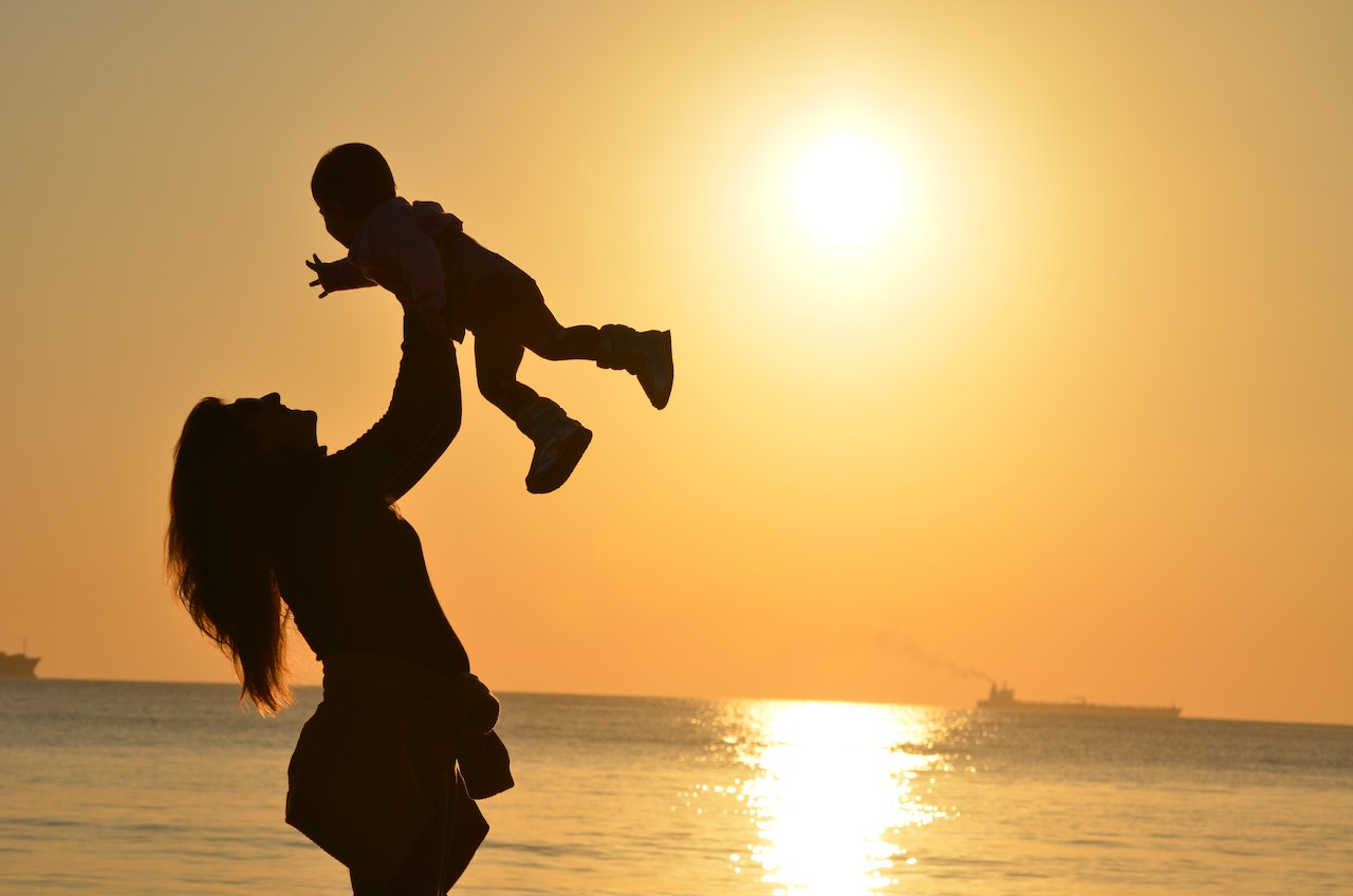 Mother throwing baby in air by sea at sunset. Full child custody in Australia. 